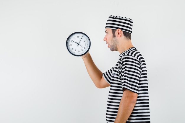 Kostenlose Foto junger mann, der auf uhr in gestreiftem t-shirt, mütze schaut und alarmiert schaut.