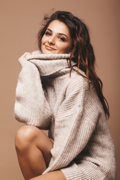 Gratis Foto portræt af smuk, sød, smilende brunette. pige i grå sweater. model poserer i studiet. sidder på en stol