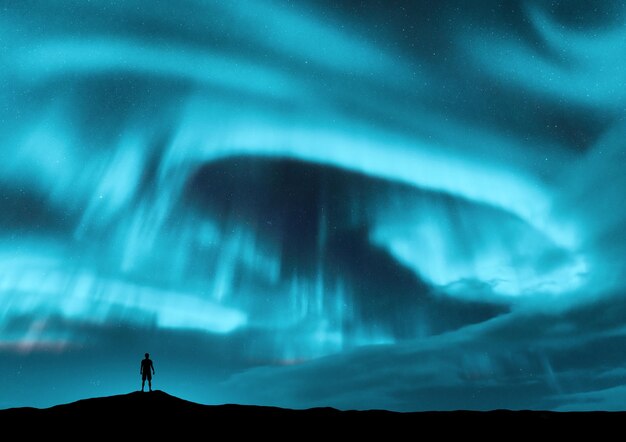 Fotoğraf tepede duran adamın aurora borealis ve silüeti lofoten adaları norveç aurora ve yalnız adam yıldızlarla dolu mavi gökyüzü ve parlak kutup ışıkları aurora ve insanlarla gece manzarası seyahat